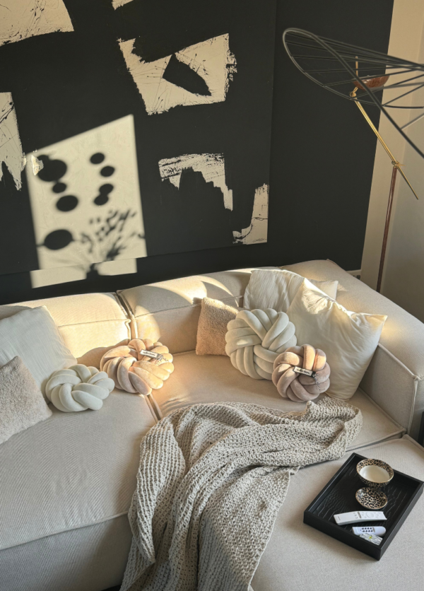 Couch, die mit handgefertigten Dekorationskissen dekoriert ist. Die Swirlkissen in der Farbe cremeweiß und hellbeige liegen auf einem beigen Sofa.