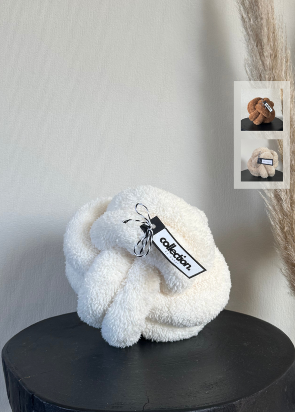 Knotenkissen aus weichem Teddystoff in cremeweiß Gr. M auf einem schwarzen Tisch. Daneben werden die weiteren Farben in einem Kästchen gezeigt. Diese sind Karamell und hellbeige