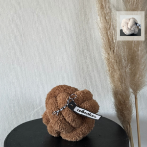 Karamellfarbenes Knotenkissen aus weichem Teddystoff mit Etikett. In einer Kachel wird die weitere Farbe "Hellbeige" gezeigt.