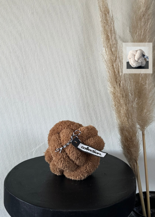 Karamellfarbenes Knotenkissen aus weichem Teddystoff mit Etikett. In einer Kachel wird die weitere Farbe "Hellbeige" gezeigt.