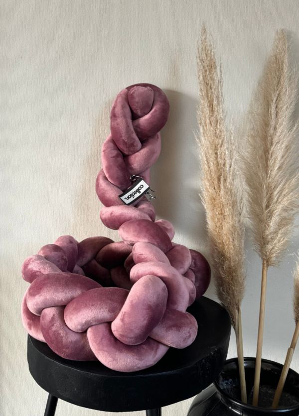 Bettschlange geflochten aus weichem Samt in altrosa. Präsentiert auf einem schwarzen Tisch, daneben steht eine Vase mit Pampasgras.