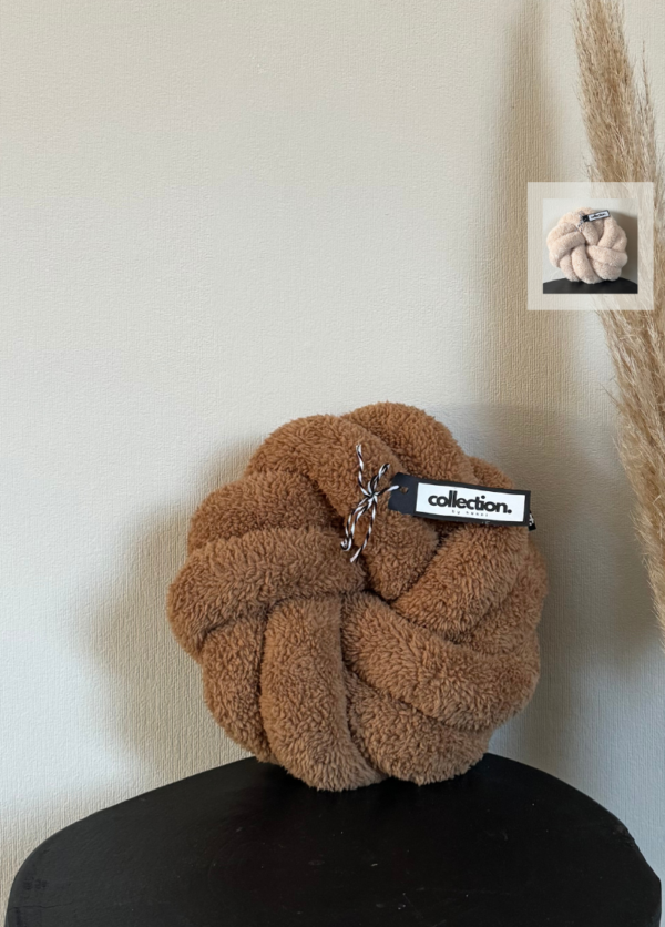 Mittleres Swirl-Knotenkissen in der Farbe Karamell. Auf den Icons links ist die weitere Farbe hellbeige zu sehen. Das Kissen wird auf einem schwarzen Tisch präsentiert.